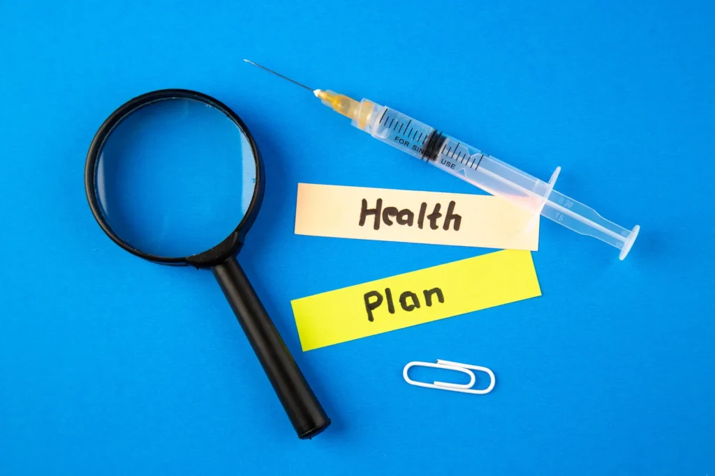 A syringe, a magnifying glass, and sticky notes labeled "Healthcare" and "Plan" on a bright blue background, next to a paperclip, illustrating a focus on advanced health planning.