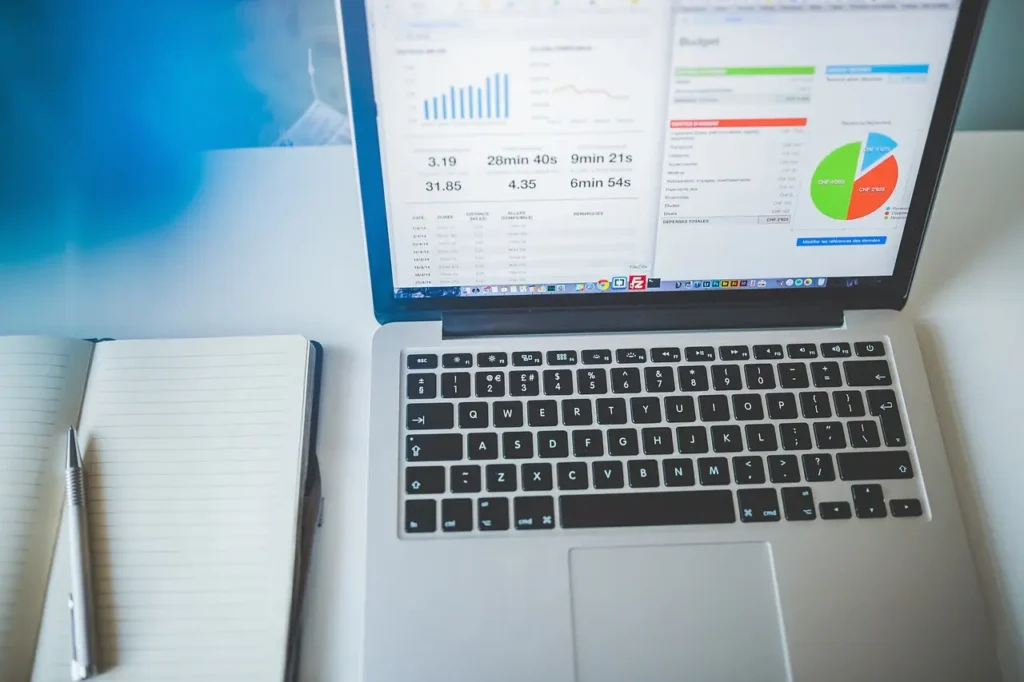 A laptop displaying healthcare data analytics on its screen with a notebook and a pen beside it on a white desk, indicating an office or study setup.